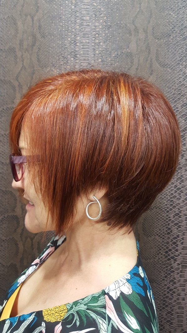 Una mujer con cabello corto y rojo lleva gafas de sol y pendientes.