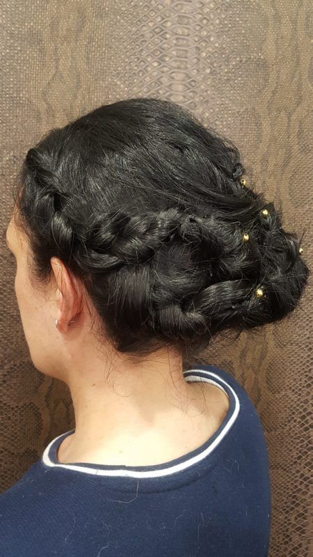 Una mujer lleva el cabello recogido en un moño trenzado con cuentas doradas.