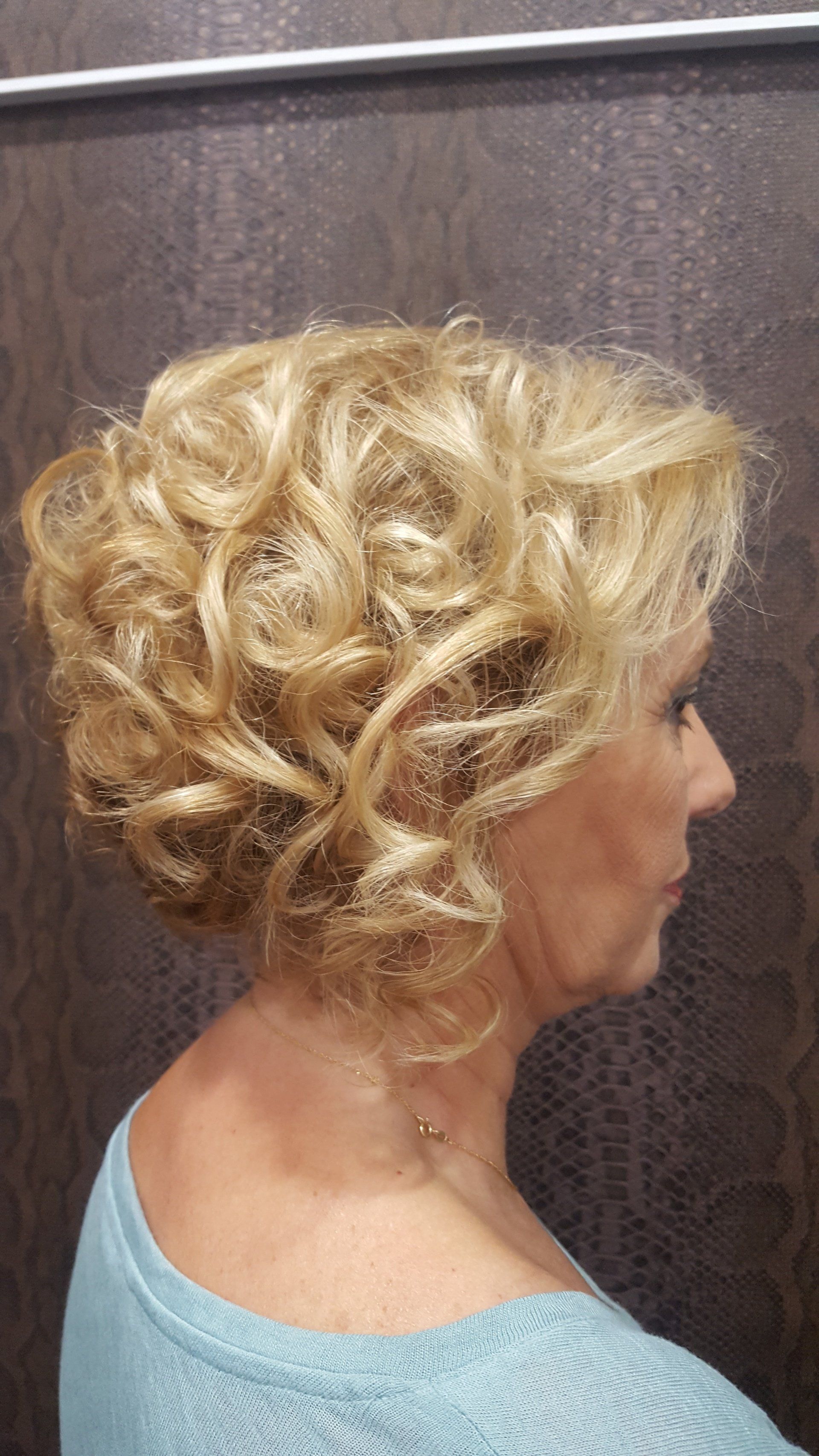 Una mujer con cabello rubio y rizado lleva un suéter azul.