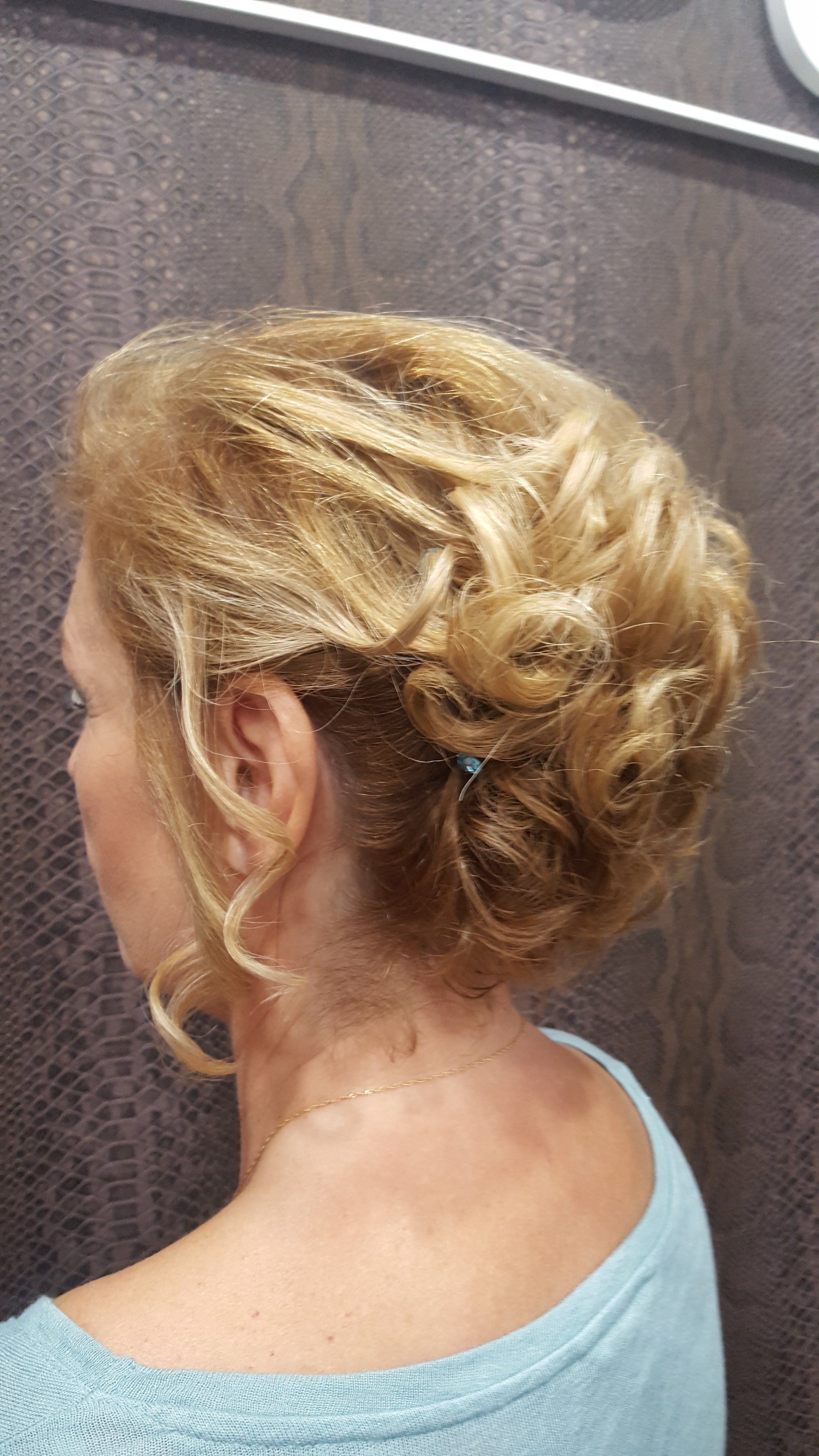 Una mujer con cabello rubio recogido en un moño lleva una camisa azul.