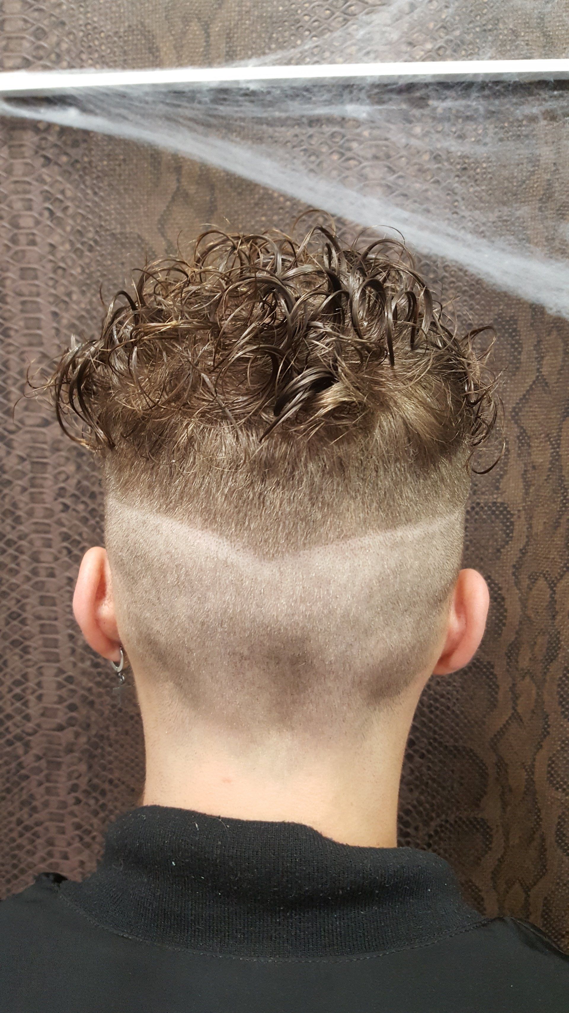 La espalda de una persona con cabello rizado y la cabeza rapada.