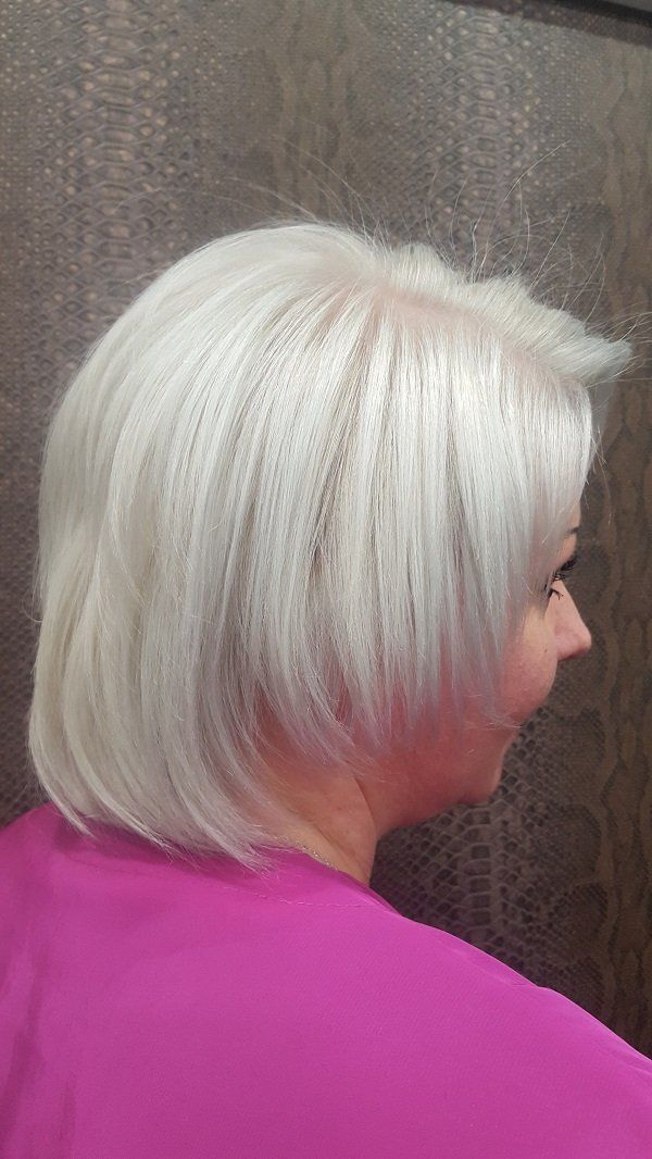 Una mujer de cabello gris lleva una camisa rosa.