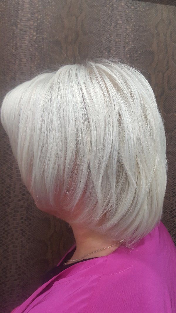 Una mujer con cabello corto y blanco lleva una camisa rosa.