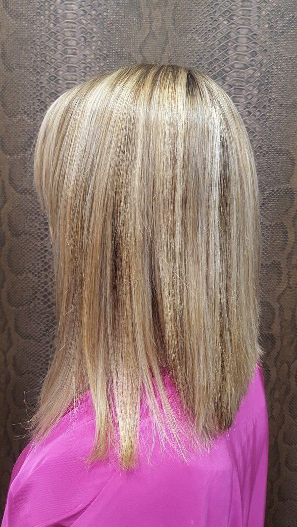 Una mujer con cabello rubio y una camisa rosa está parada frente a una pared.