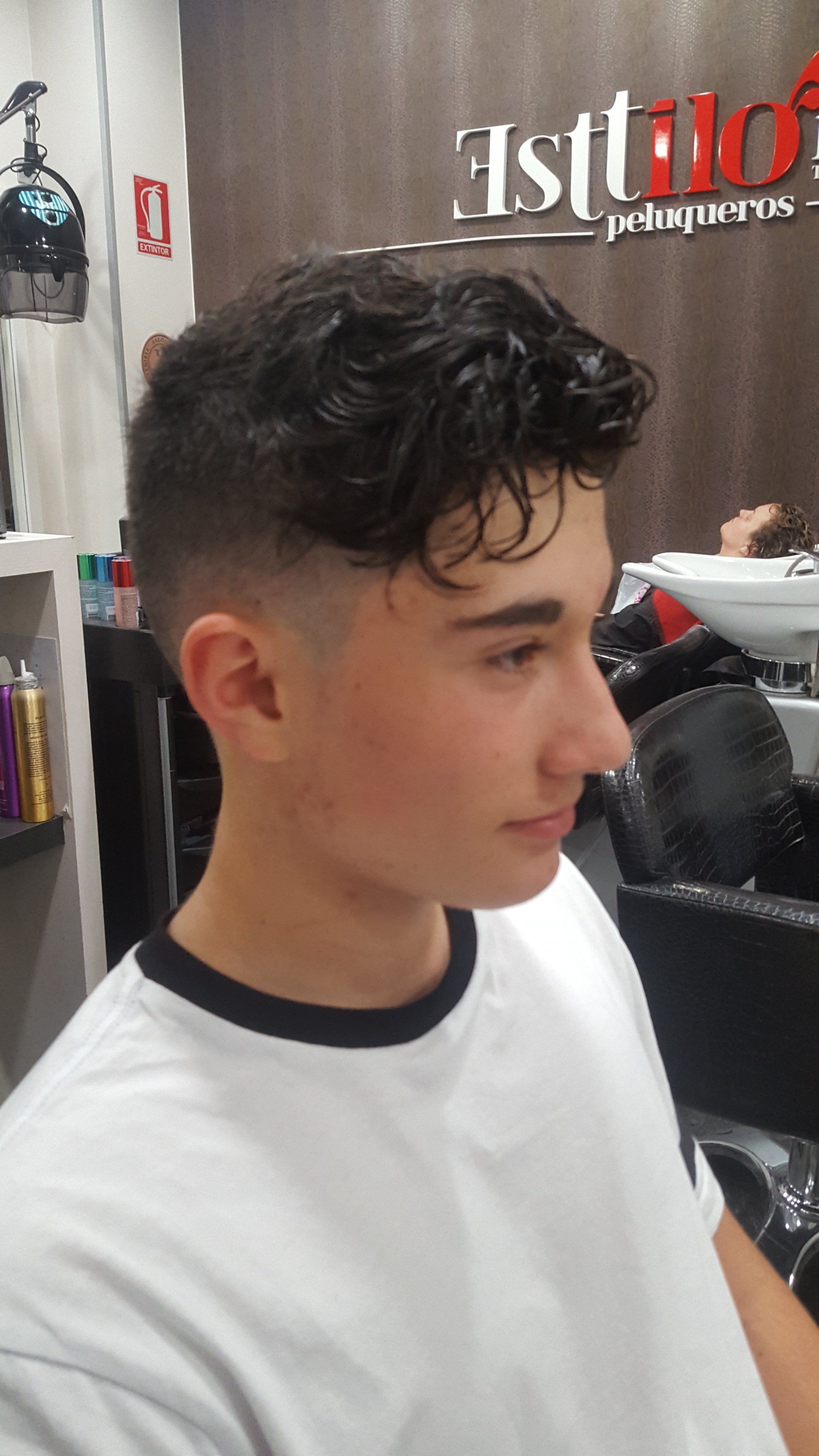 Un joven con cabello rizado se está cortando el pelo en una peluquería.