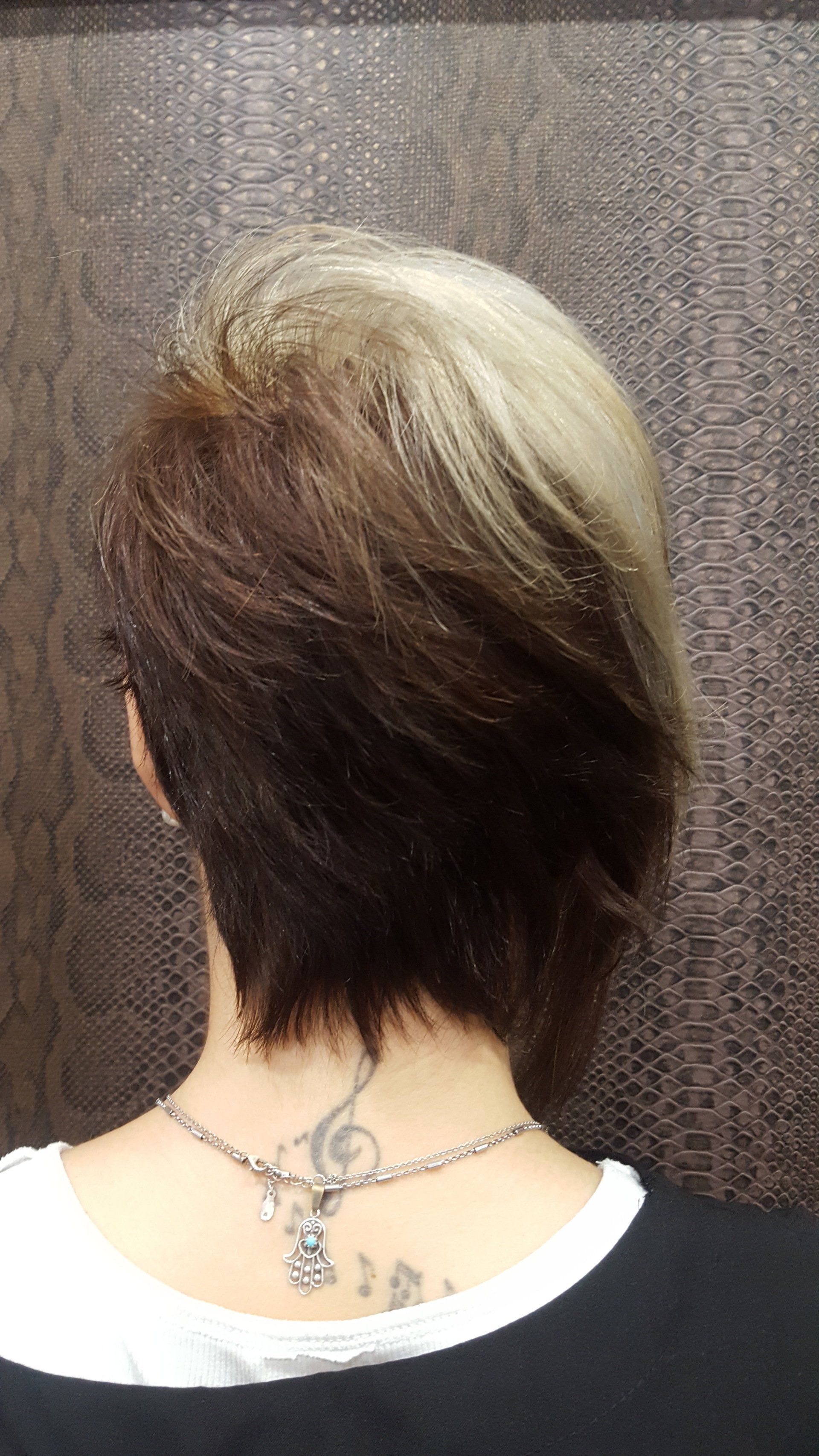 La parte posterior de la cabeza de una mujer con cabello corto y un tatuaje en el cuello.