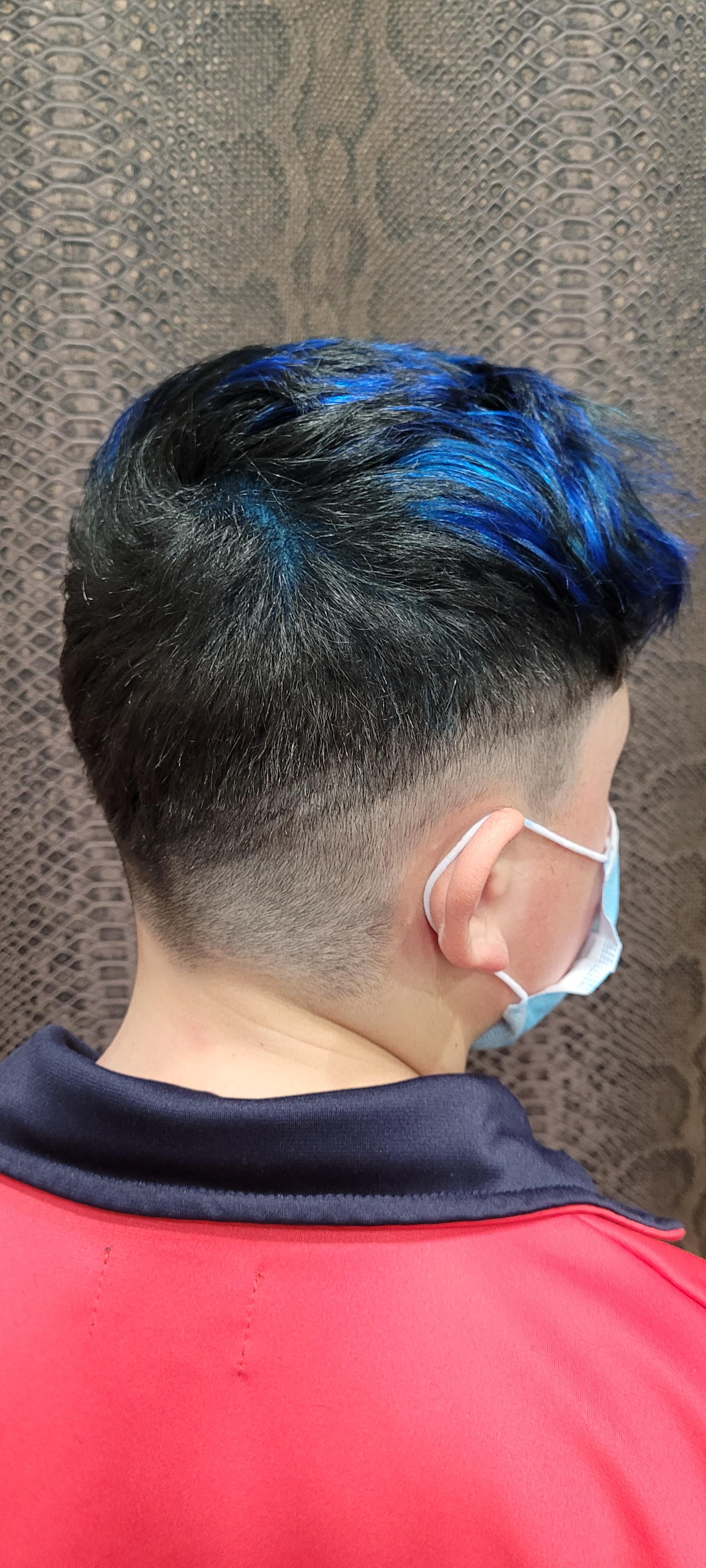 Un hombre con cabello azul lleva una máscara y una camisa roja.