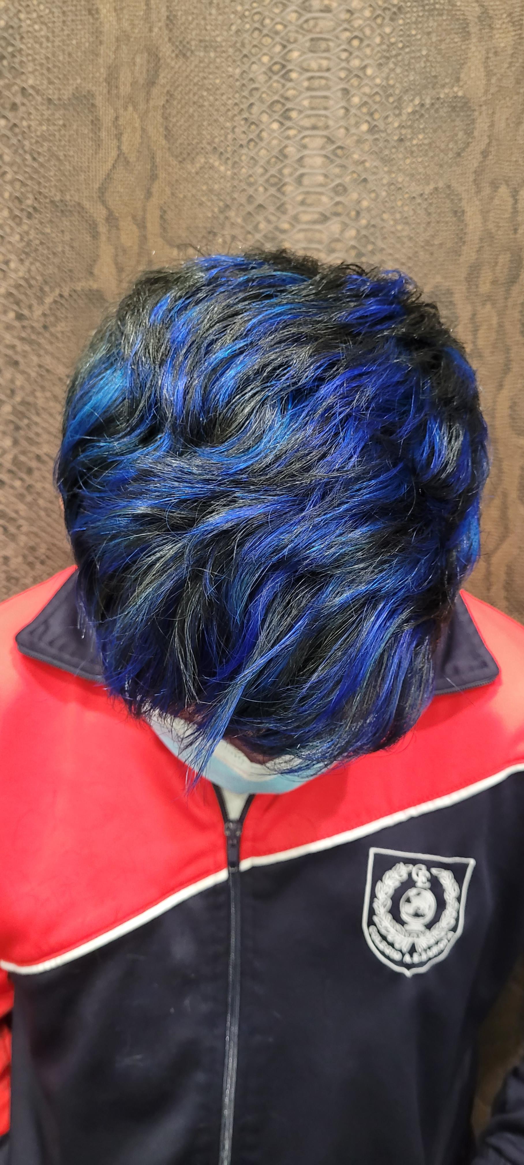 Una persona con cabello azul lleva una chaqueta roja y azul.