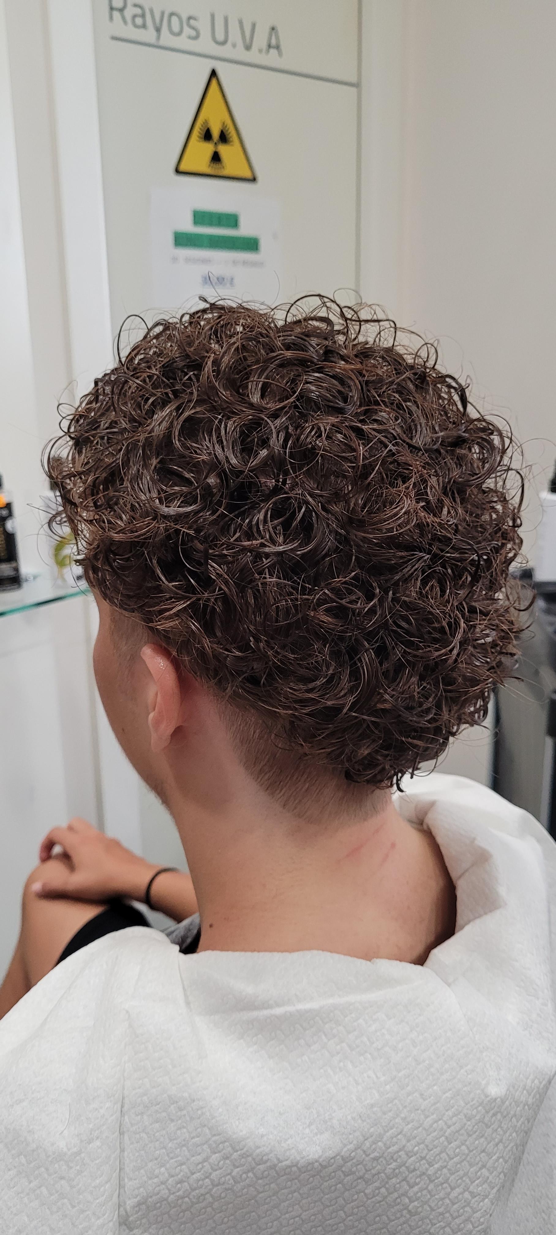 Un hombre con cabello rizado se está cortando el pelo en una peluquería.