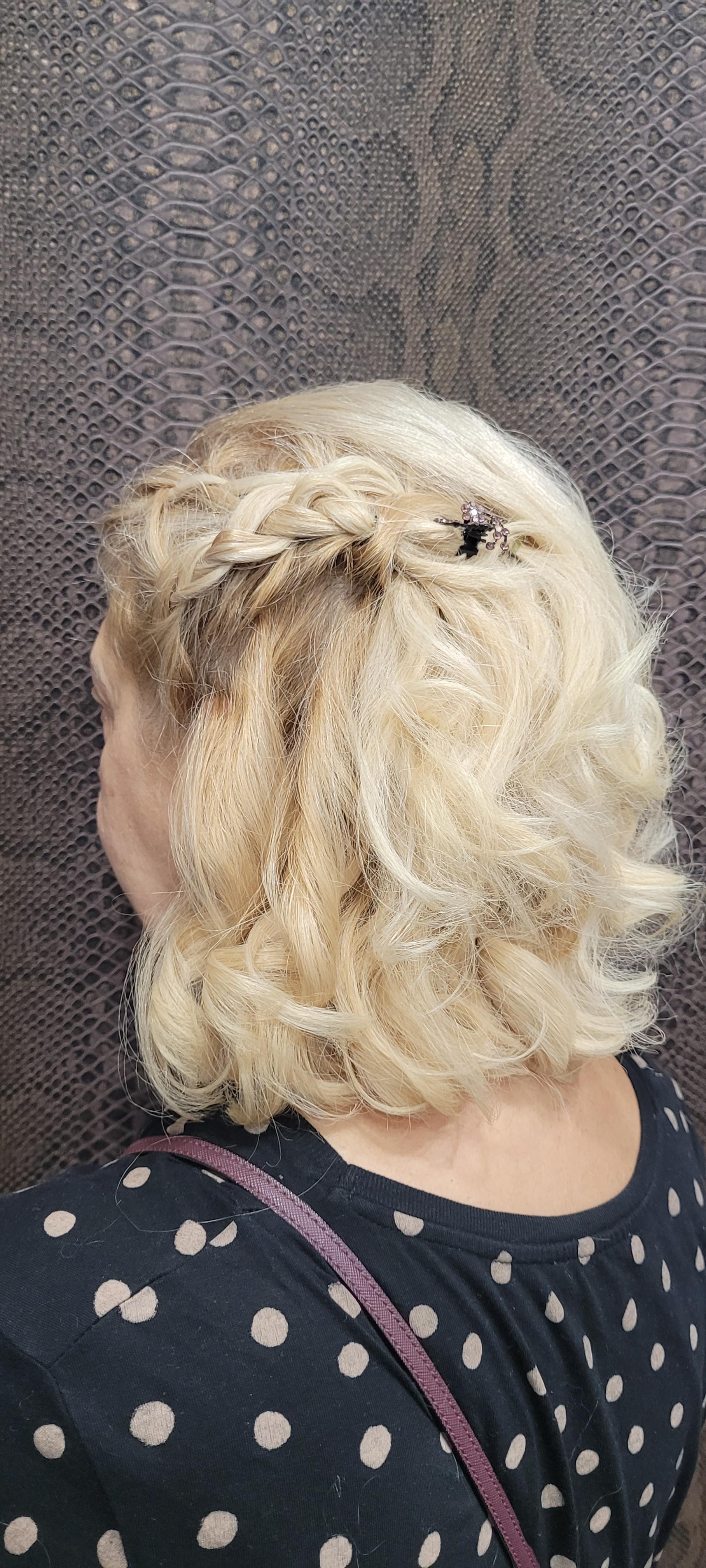 Una mujer con cabello rubio y una camisa de lunares está parada frente a una pared.