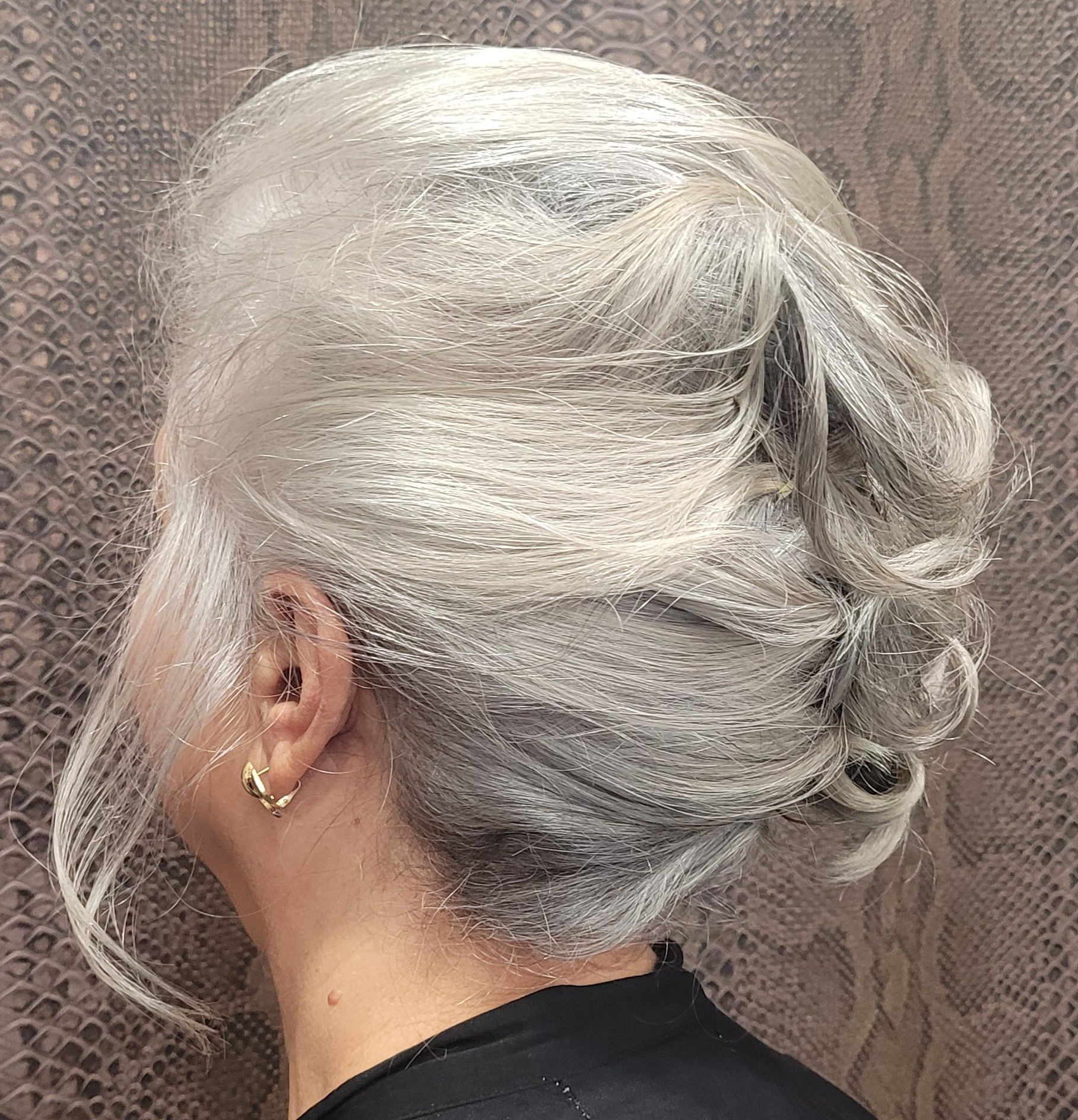 Una mujer de cabello gris lleva una camisa negra y pendientes.