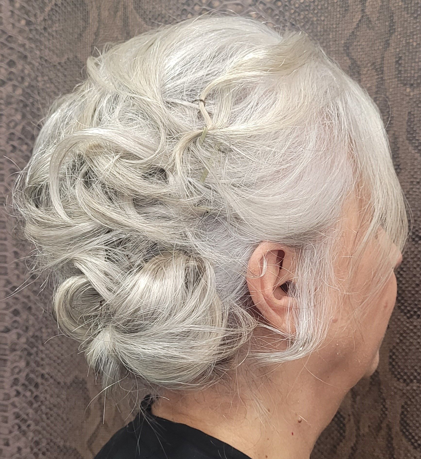 Una mujer de cabello gris lleva una camisa negra y tiene el pelo recogido en un moño.