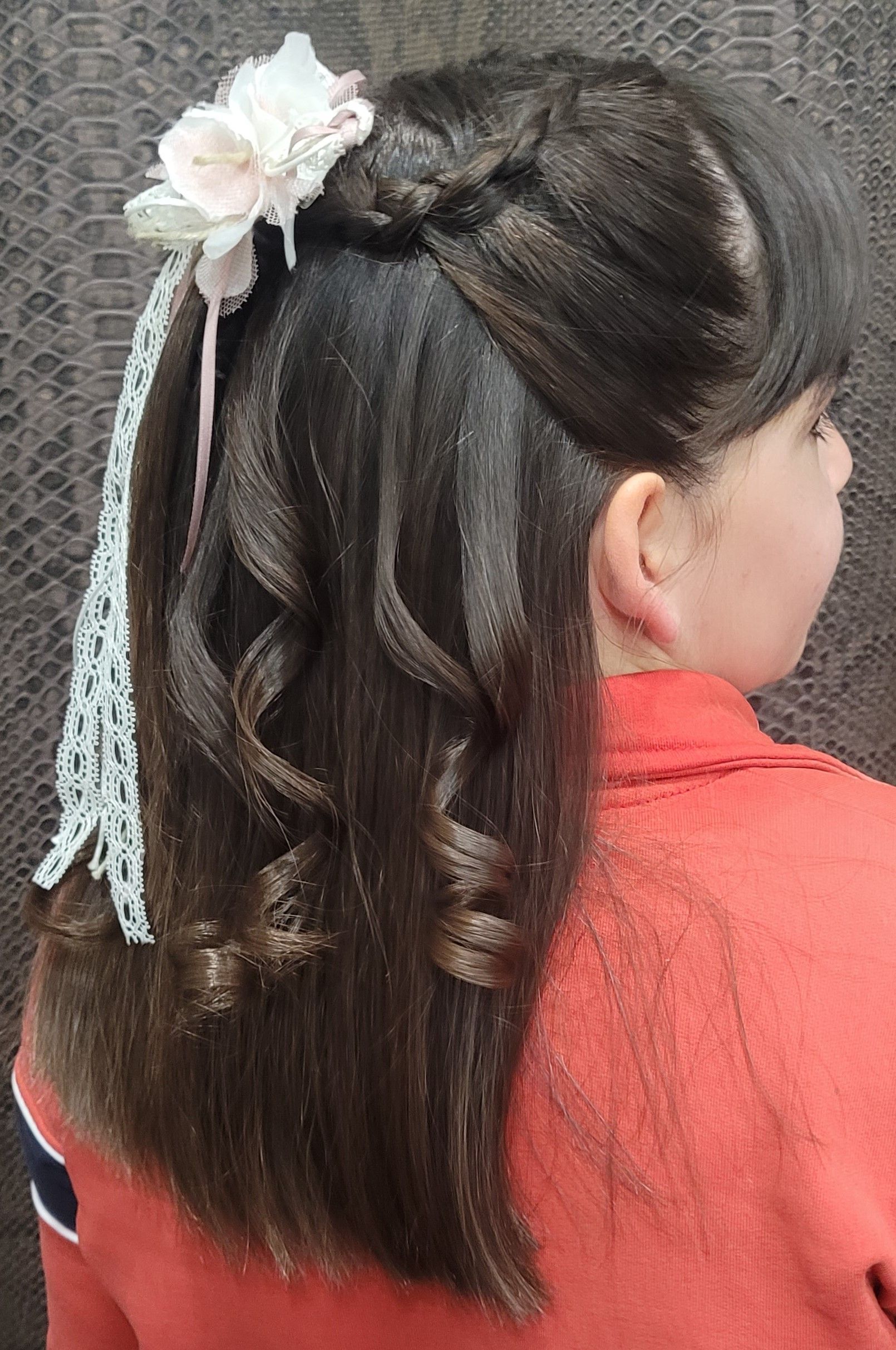 Una niña lleva una cola de caballo trenzada con una flor en el pelo.