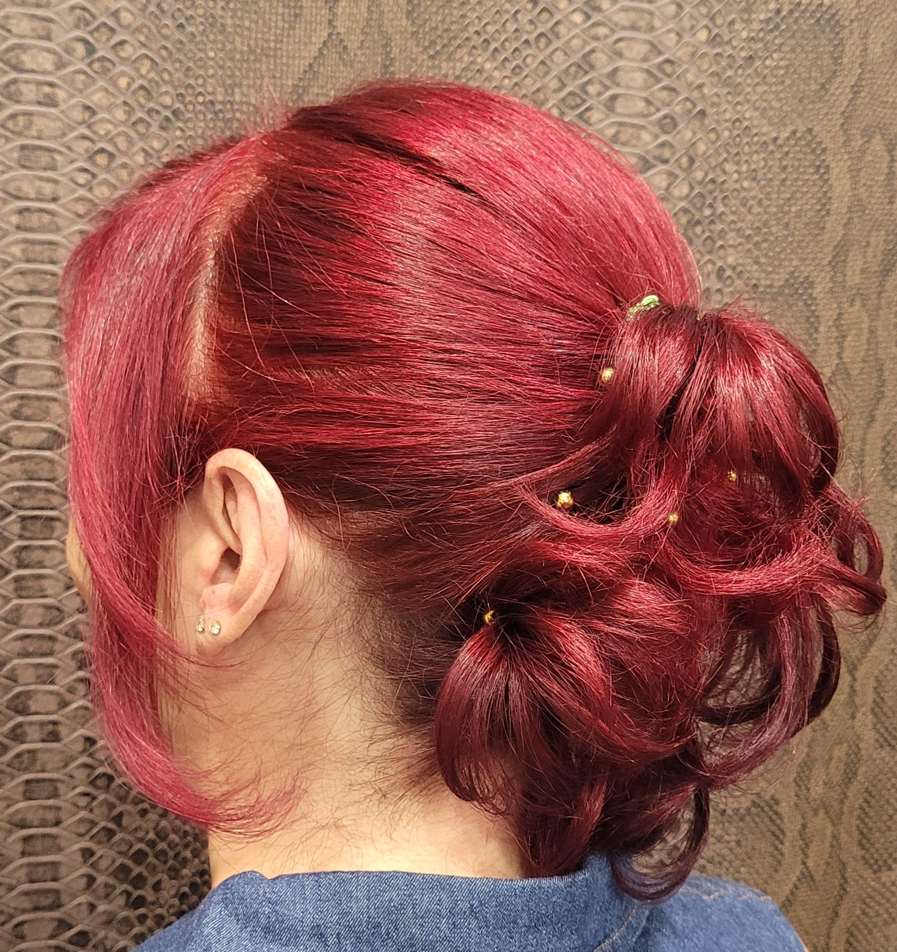 Una mujer con cabello rojo lleva una camisa azul y tiene el cabello recogido en un moño.