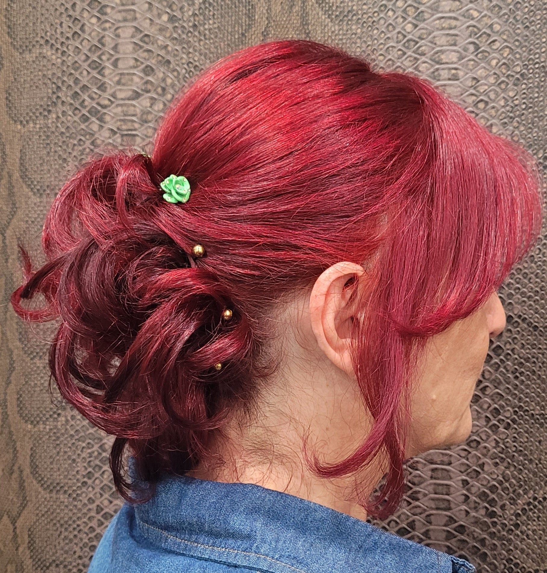 Una mujer con cabello rojo lleva una camisa azul y tiene una flor en el cabello.