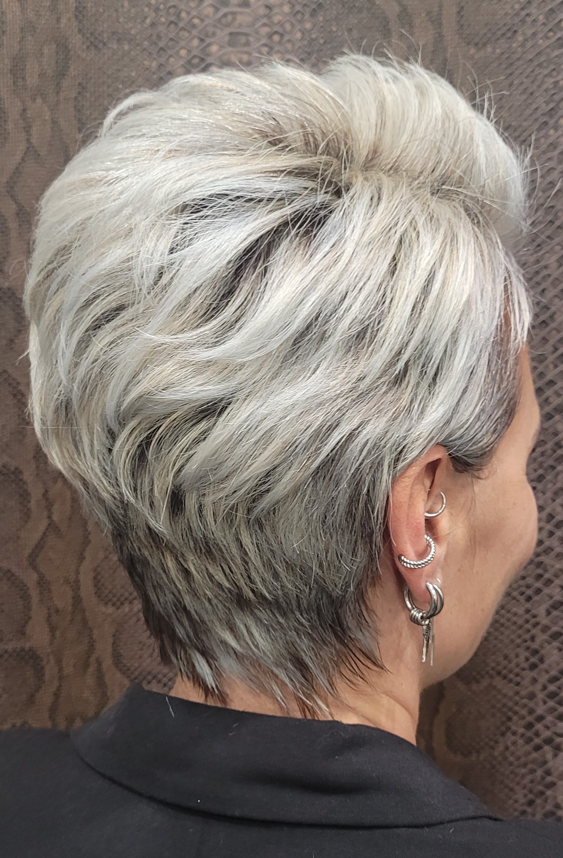 Una mujer con pelo corto gris y pendientes lleva una camisa negra.