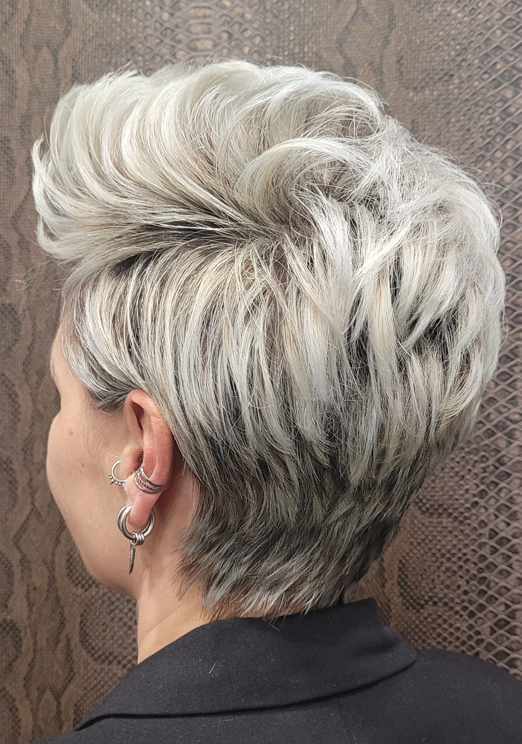 Una mujer con pelo corto blanco y pendientes lleva una chaqueta negra.