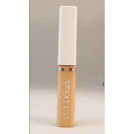 Un tubo de corrector Dekade reposa sobre una superficie blanca.