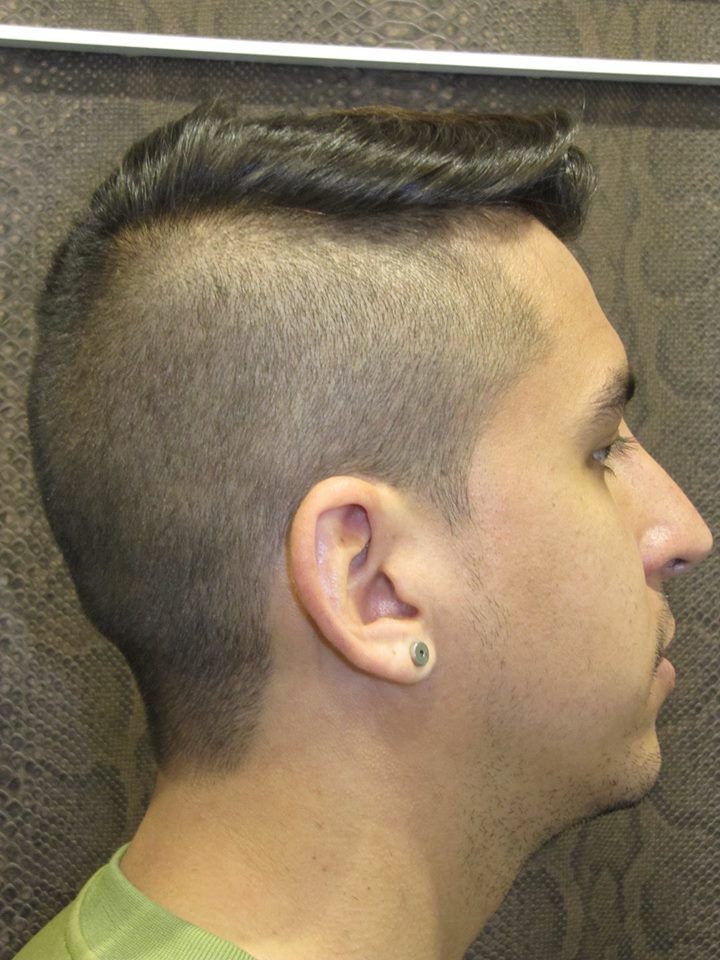 El hombre lleva una camisa verde y tiene un peinado mohawk.