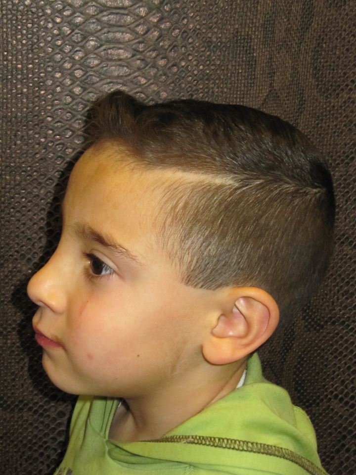 Un niño pequeño con un lado afeitado lleva una camisa verde.