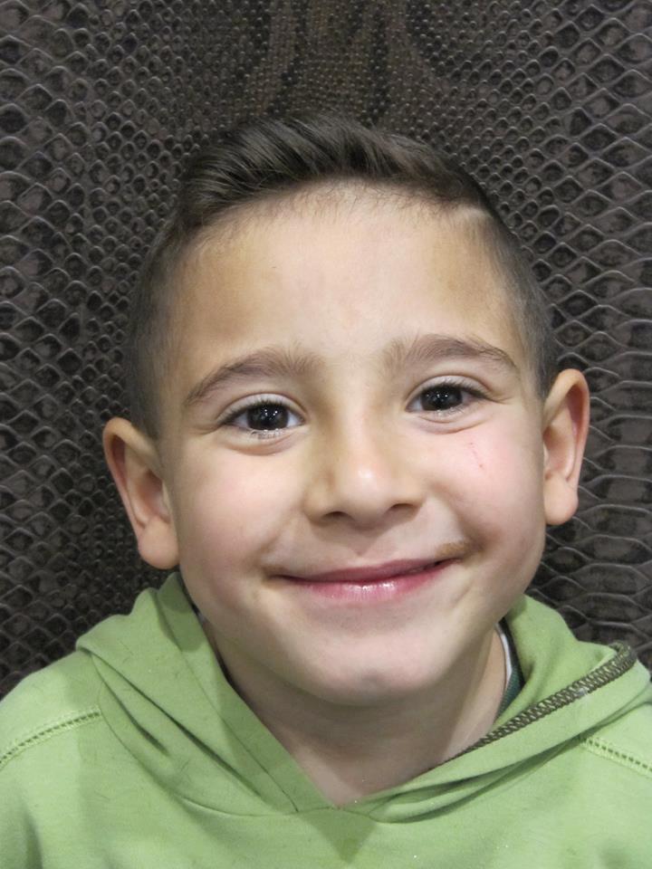 Un niño pequeño que lleva una sudadera con capucha verde sonríe a la cámara.