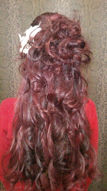 Una mujer con cabello rojo y rizado lleva un suéter rojo y tiene una flor en el cabello.
