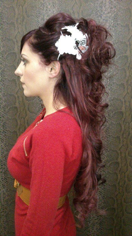 Una mujer con cabello largo y rojo lleva un vestido rojo y una flor blanca en el cabello.