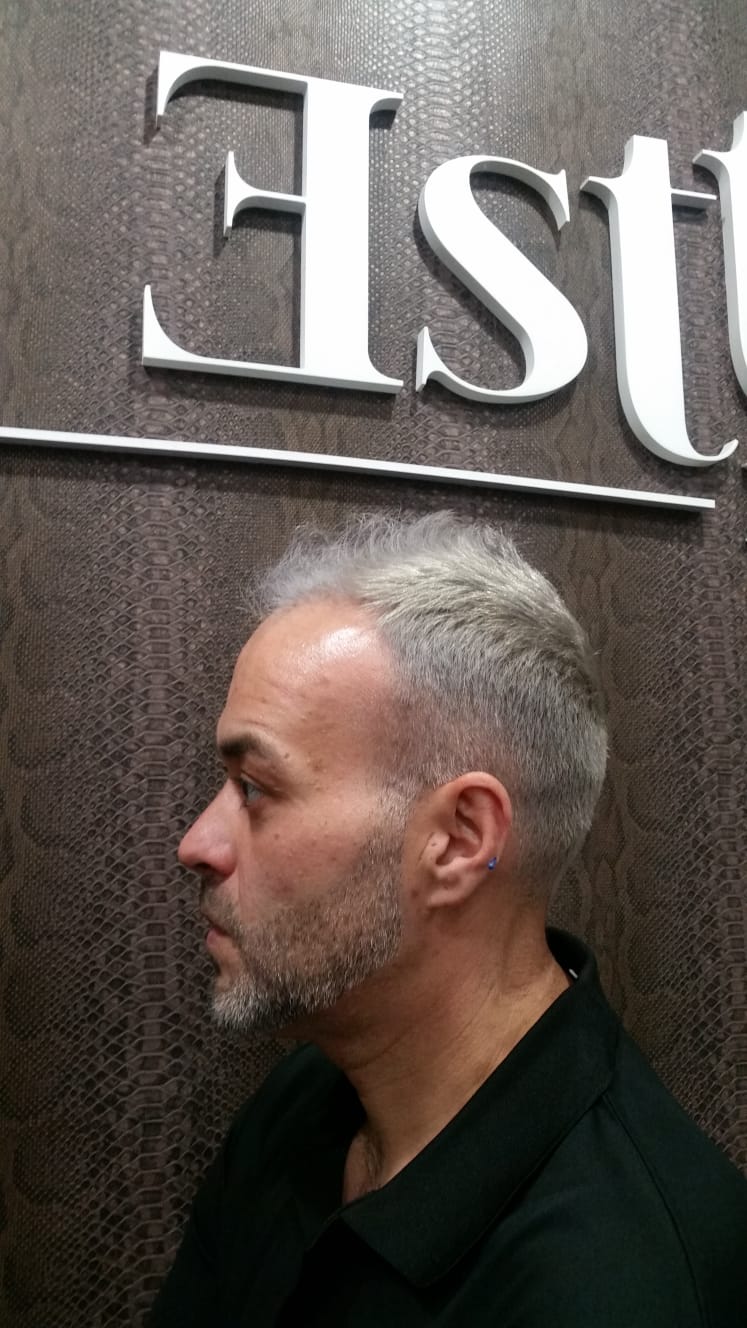 Un hombre con cabello gris y barba está parado frente a un cartel que dice est.