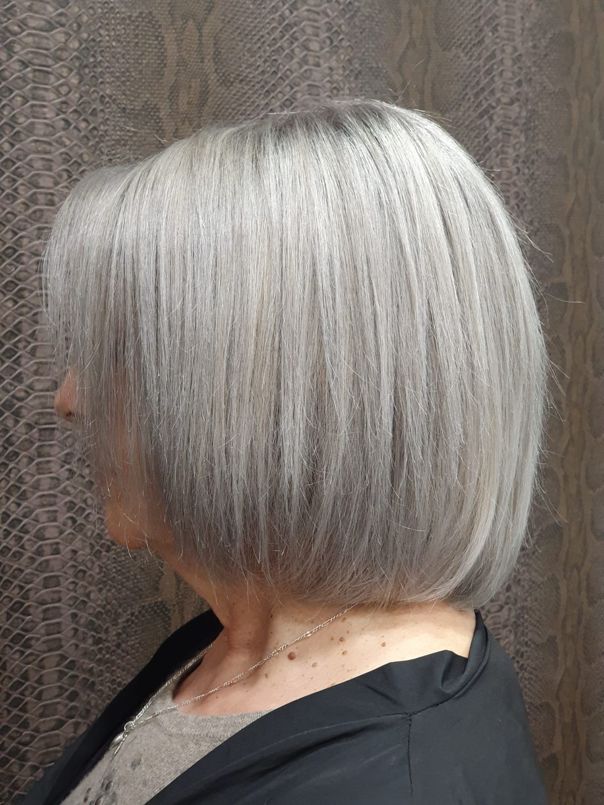 Una mujer de cabello gris lleva una chaqueta negra y un collar.