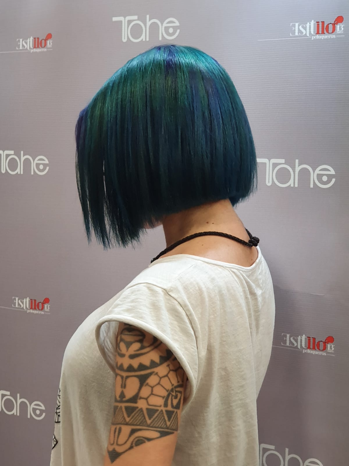 Una mujer con cabello azul lleva una camisa blanca y tiene un tatuaje en el brazo.