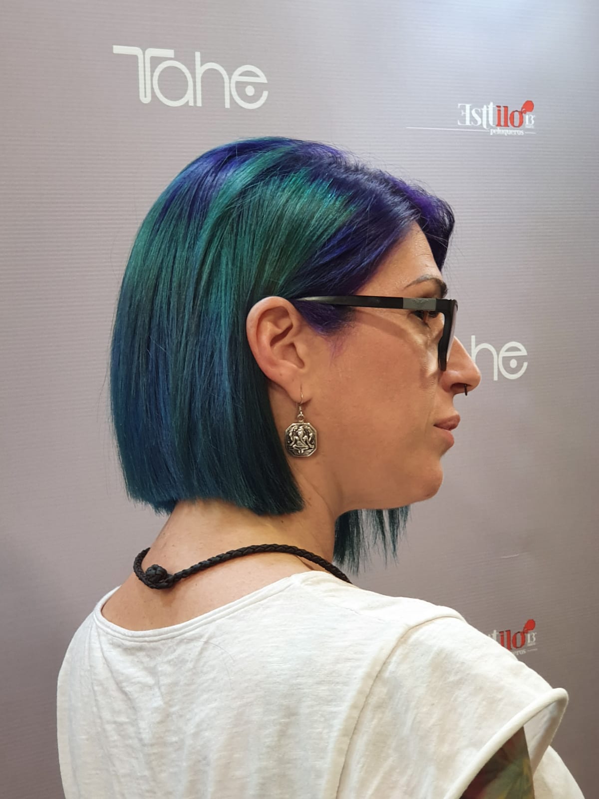 Una mujer con cabello verde y morado lleva gafas.