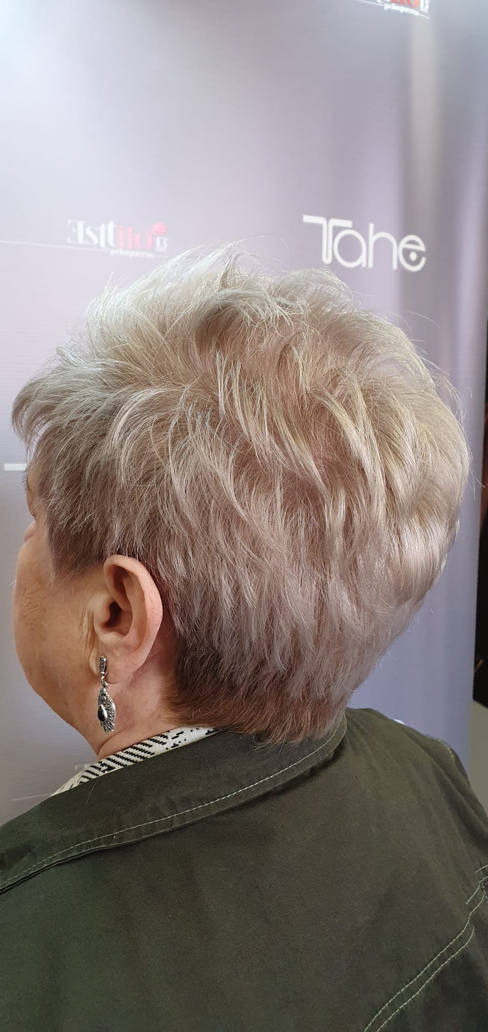 Una mujer con pelo corto y pendientes lleva una chaqueta verde.