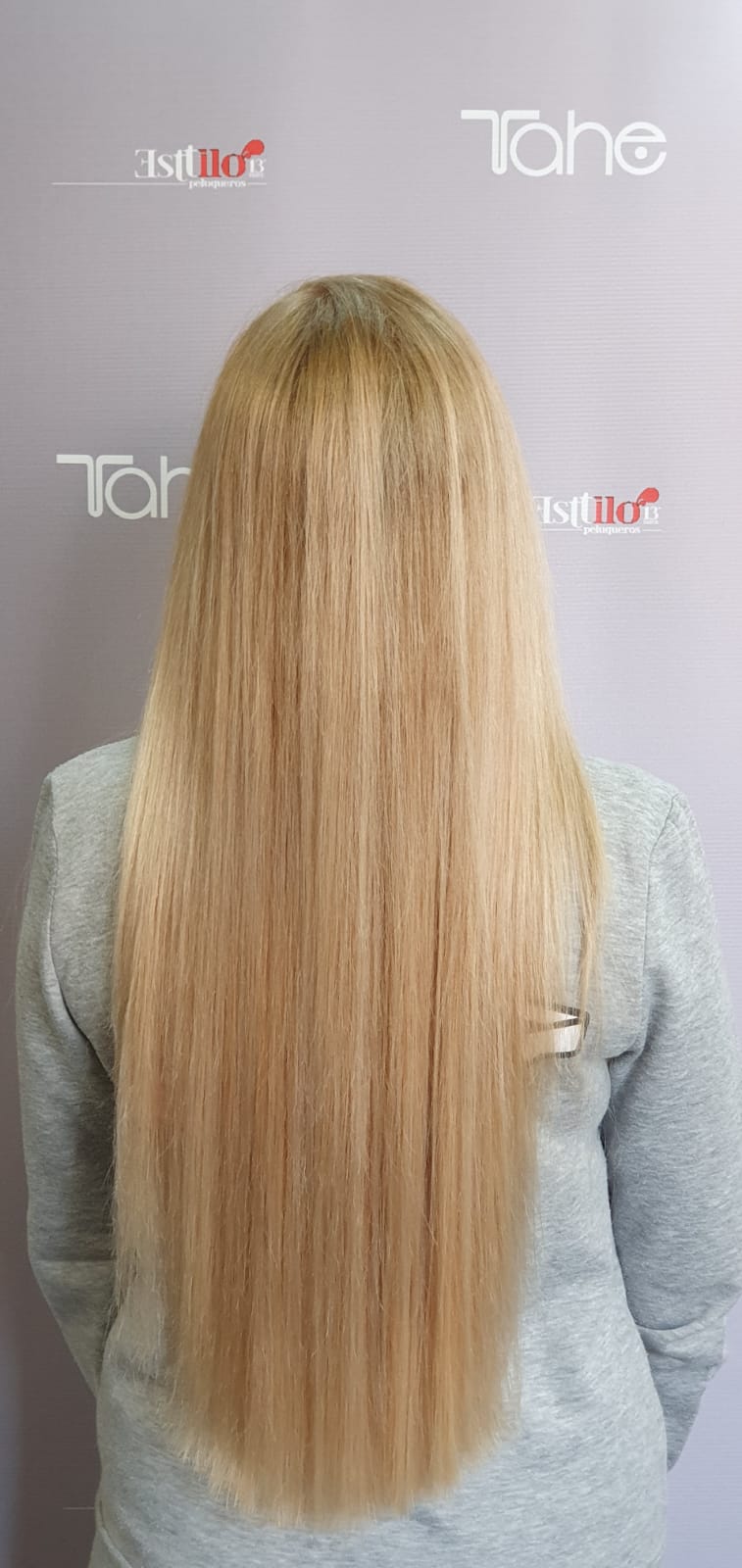 Una mujer con cabello rubio muy largo está parada frente a una pared.