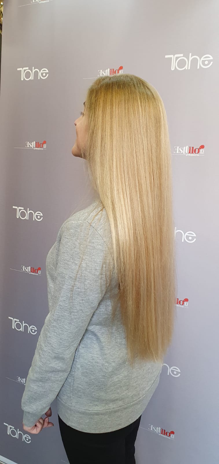 Una mujer con cabello largo y rubio está parada frente a una pared.