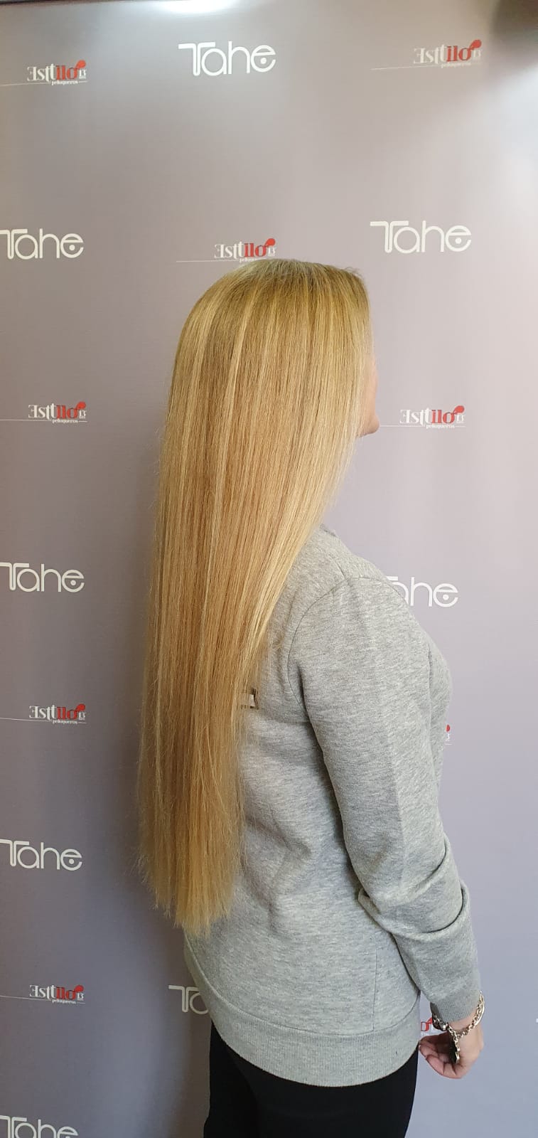 Una mujer con cabello rubio muy largo está parada frente a una pared.