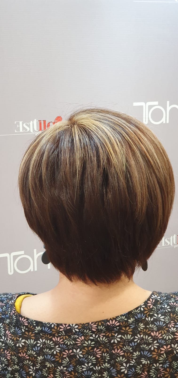 La parte posterior de la cabeza de una mujer con cabello corto y una camisa floreada.