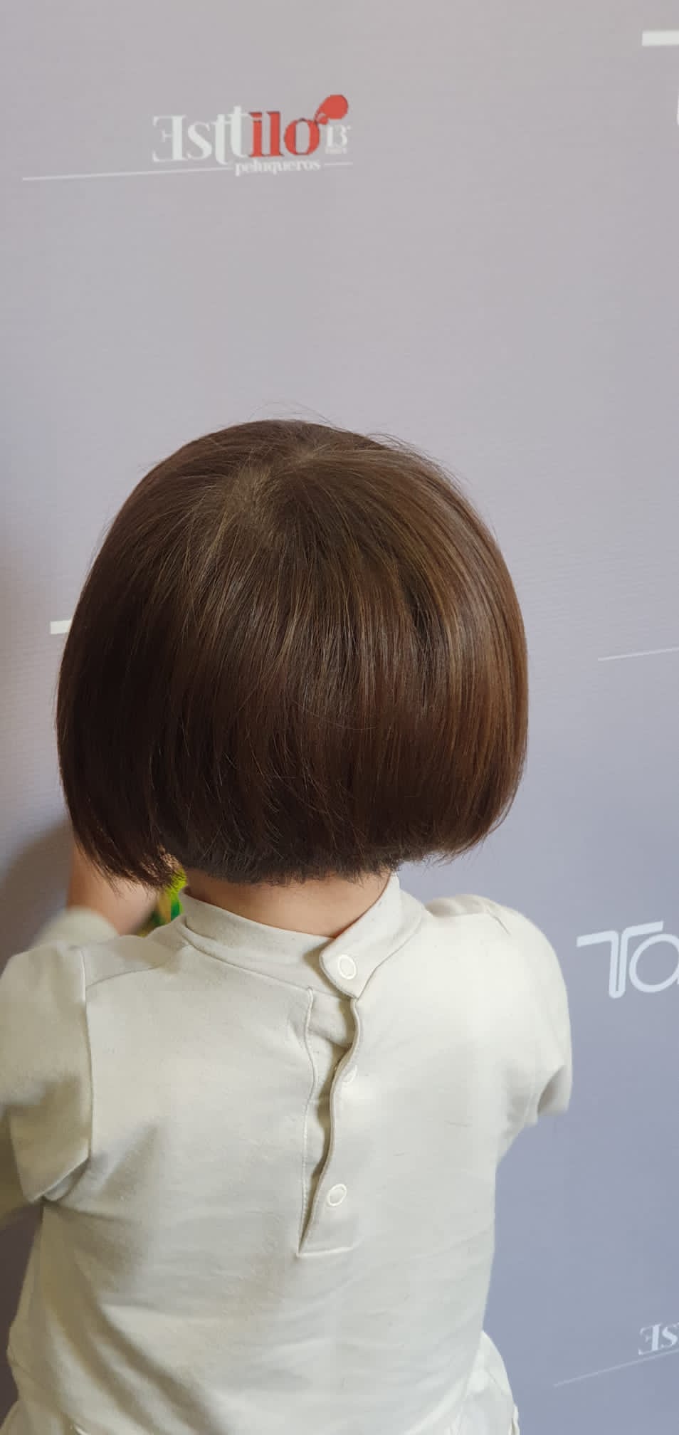 Una niña con cabello corto y castaño está parada frente a una pared.