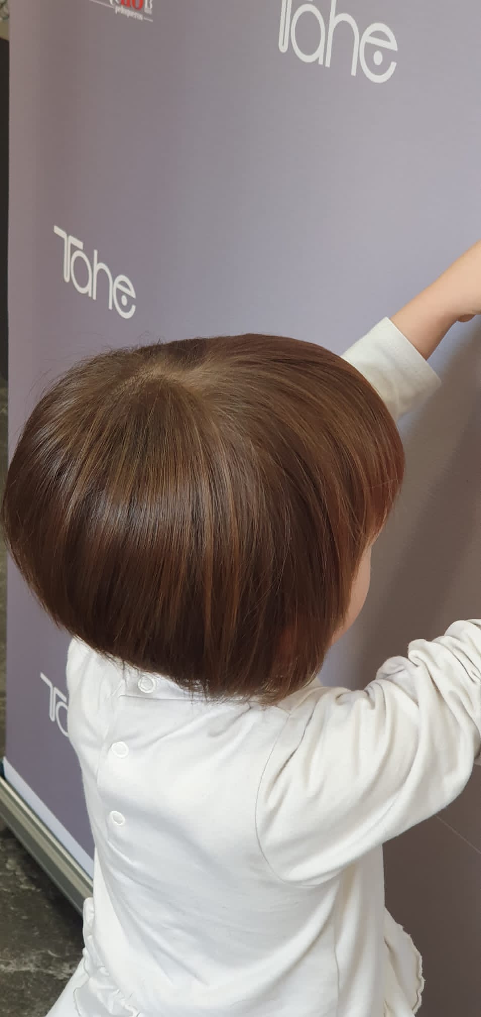 Una niña con un peinado bob está parada frente a una pared violeta.