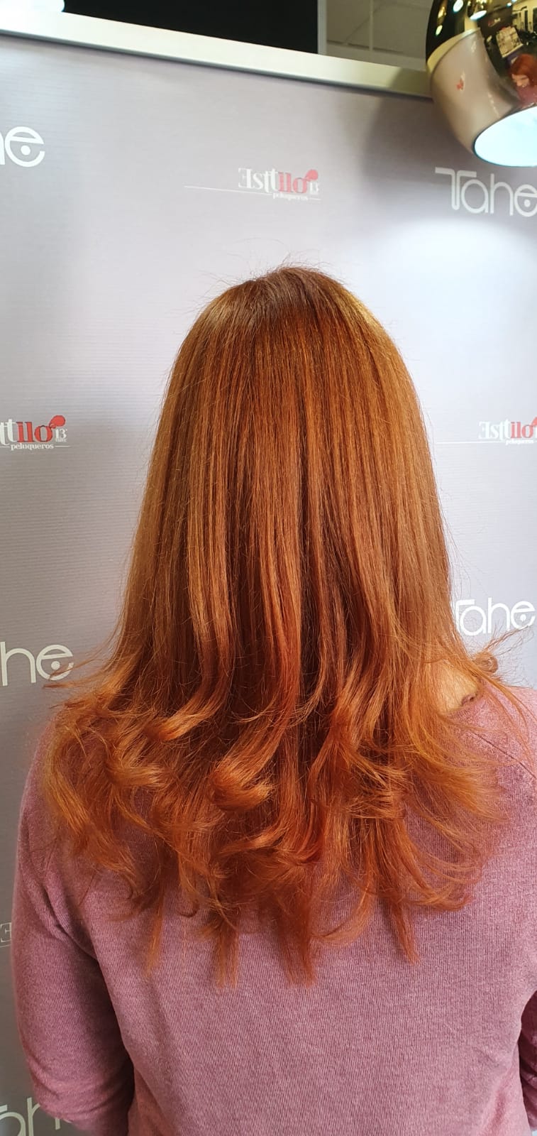 Una mujer con cabello largo y rojo está parada frente a una pared.