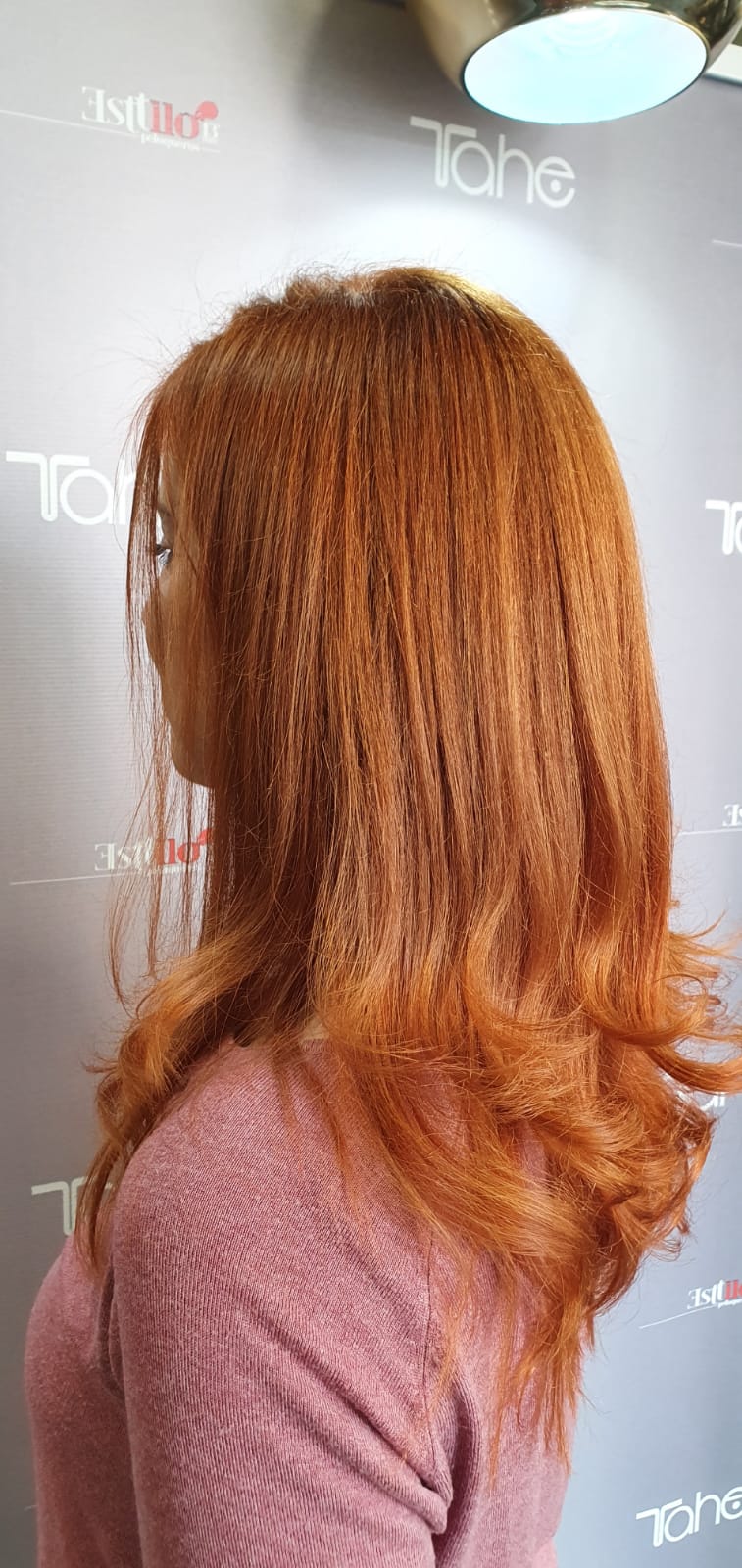 Una mujer con cabello largo y rojo está parada frente a una pared.