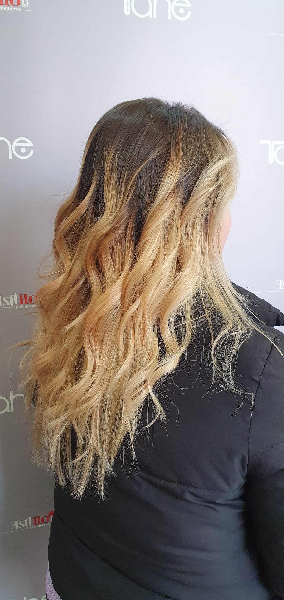 Una mujer con cabello largo y rubio está parada frente a una pared.