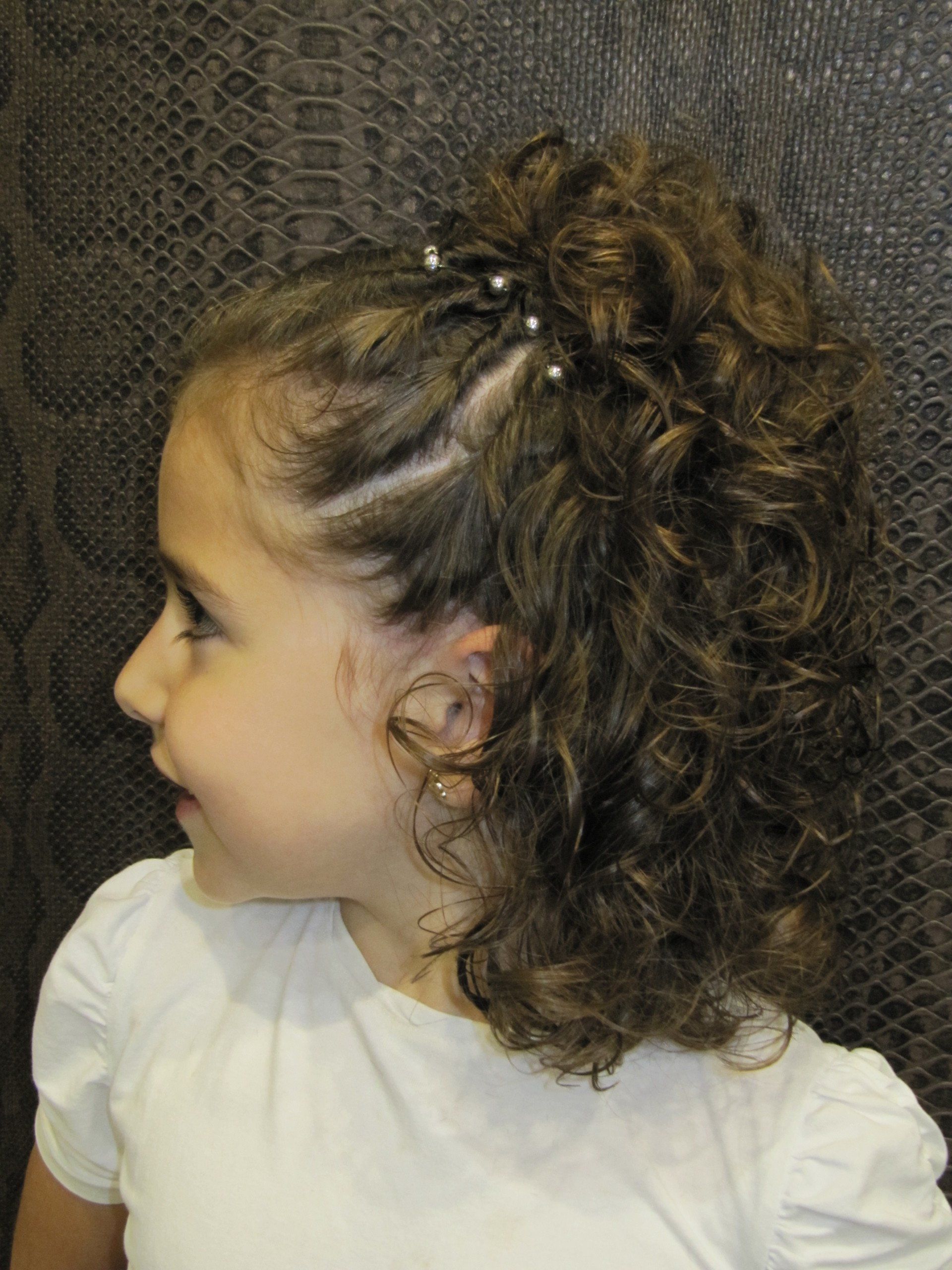 Una niña con cabello rizado lleva una camisa blanca.