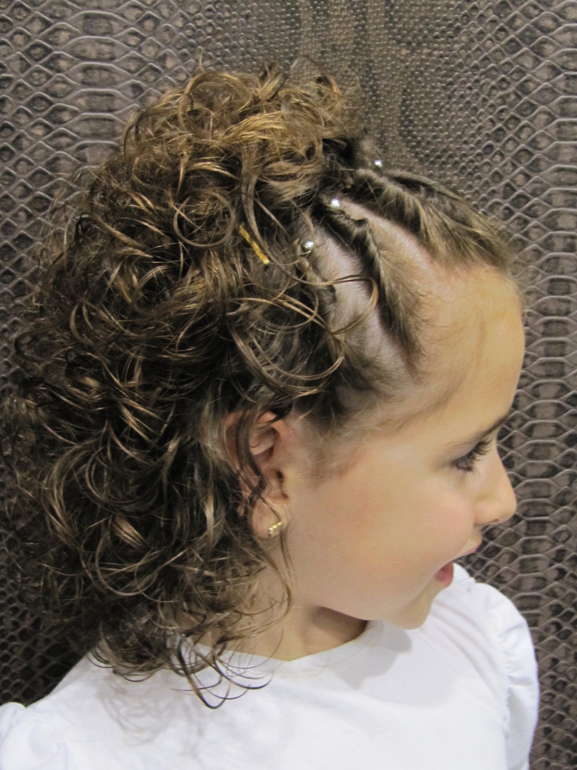 Una niña con cabello rizado lleva una camisa blanca.