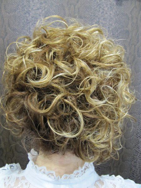 Una mujer con cabello rubio y rizado lleva una camisa blanca.