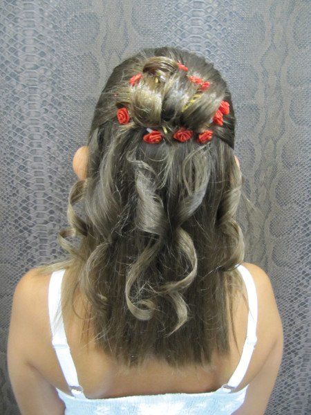 Una mujer lleva un peinado trenzado con flores rojas en el cabello.