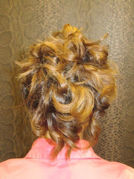 Una mujer lleva una túnica rosa y tiene el cabello recogido en un moño desordenado.