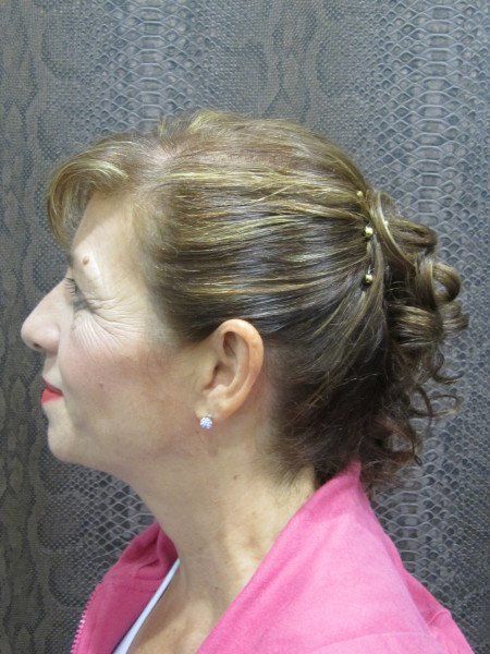 Una mujer con una camisa rosa tiene el pelo recogido en un moño.