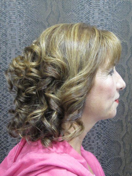 Una mujer con cabello rizado lleva una camisa rosa.