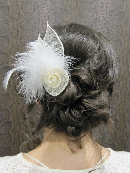 Una mujer lleva un moño con una flor blanca y plumas en el pelo.