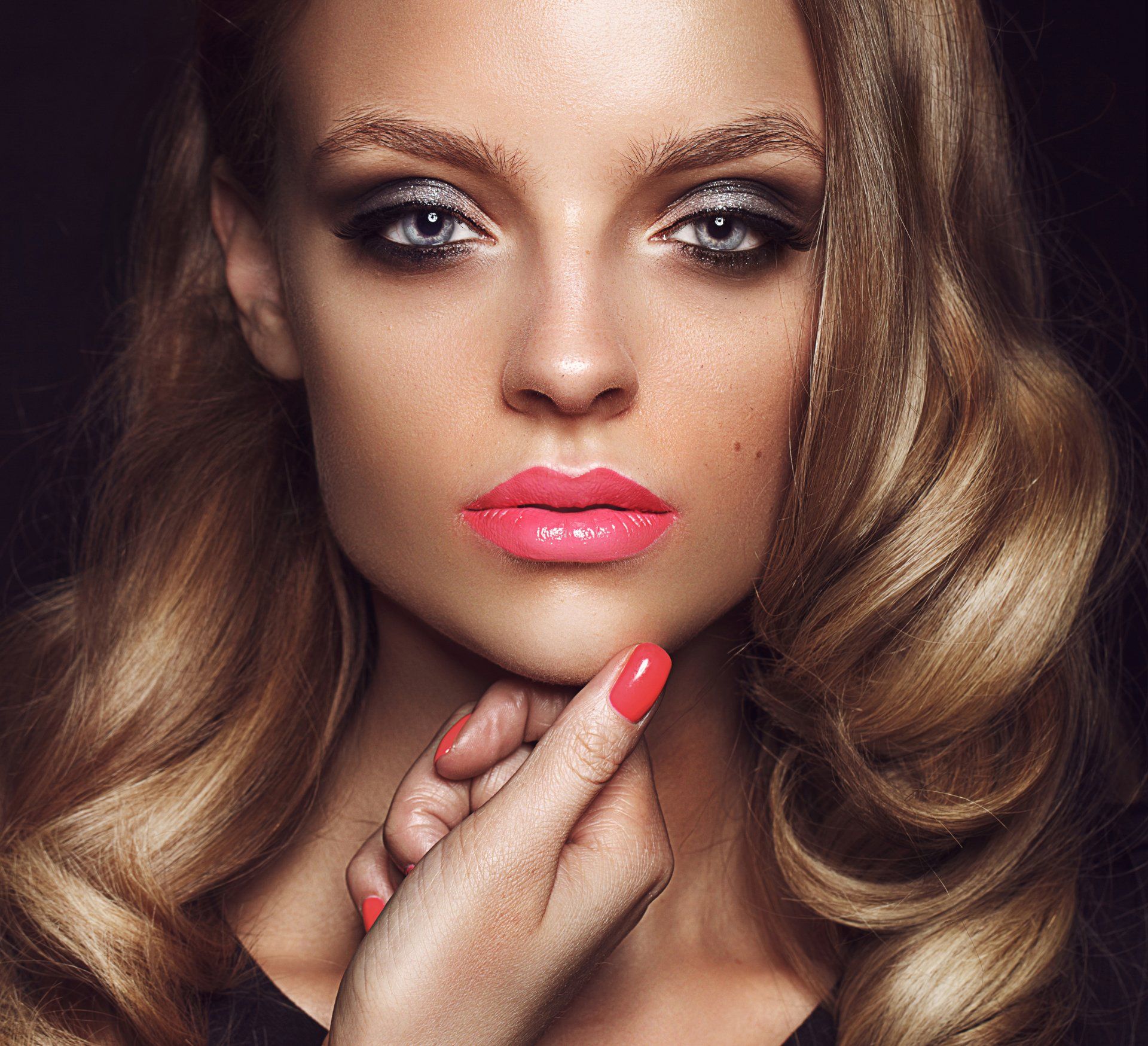 Un primer plano del rostro de una mujer con uñas rojas y labios rosados.